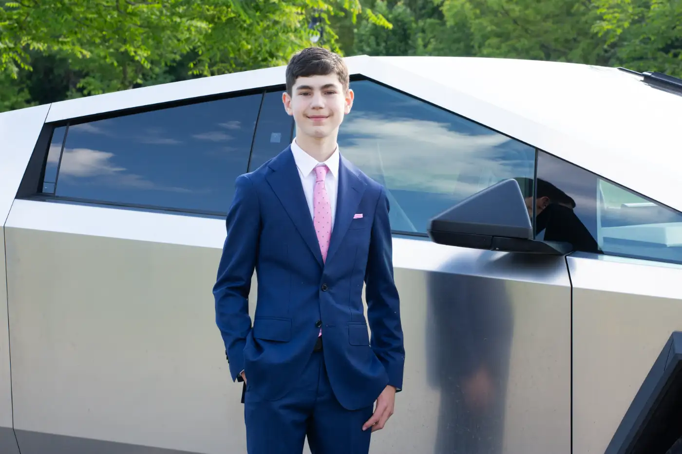 Evan Uster standing beside a Tesla Cybertruck in a navy suit
